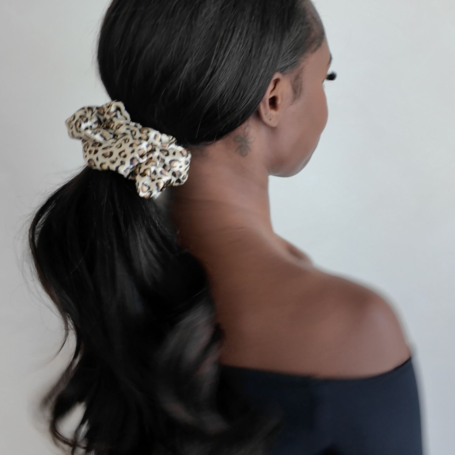 Woman with a leopard print scrunchie in her hair against a neutral background