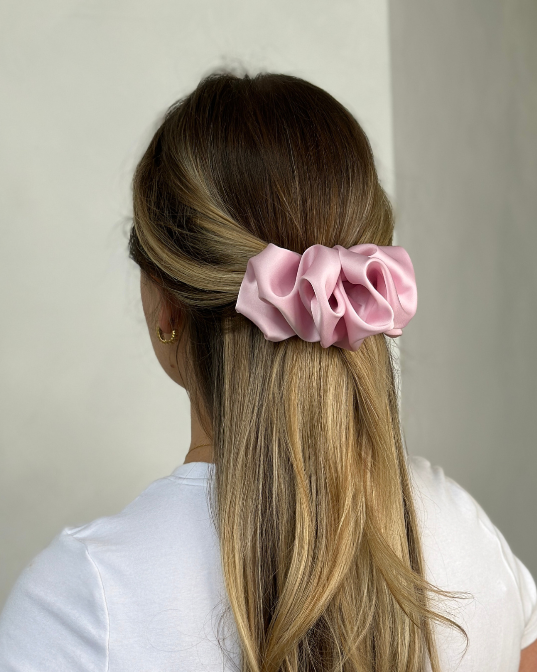 Person with pink scrunchie in hair against a plain background
