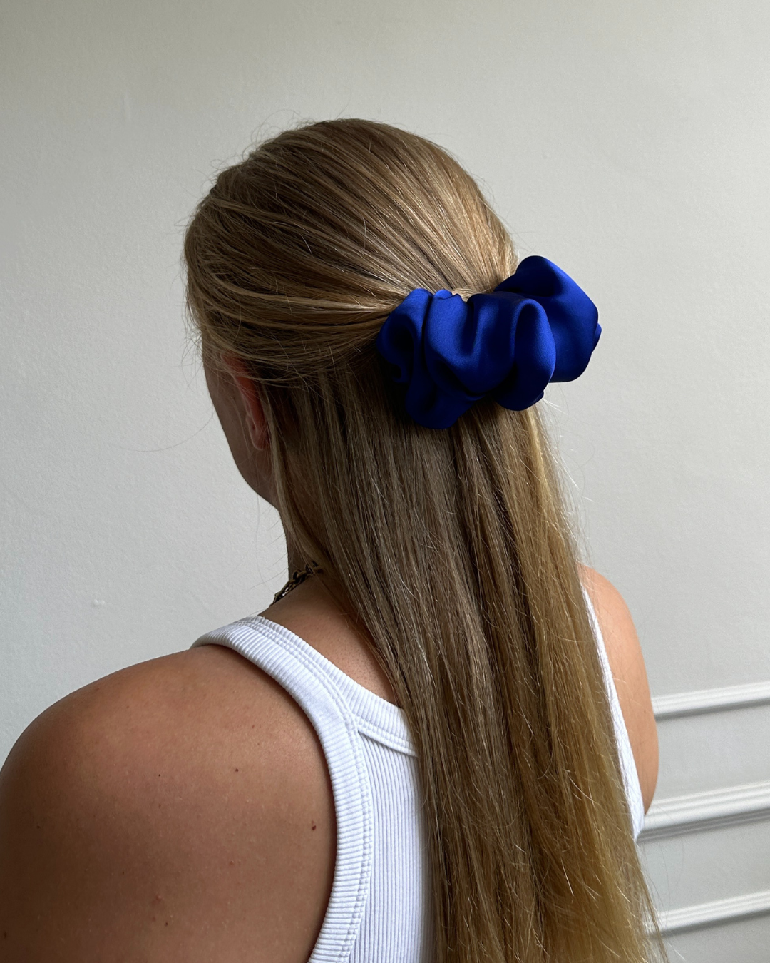 Person with long hair wearing a blue scrunchie against a plain background